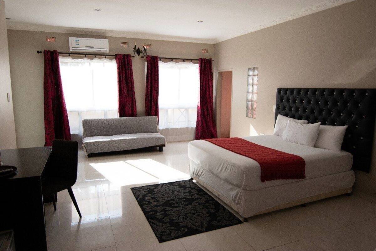A bedroom with a bed, a sofa, a desk, and a window with curtains.
