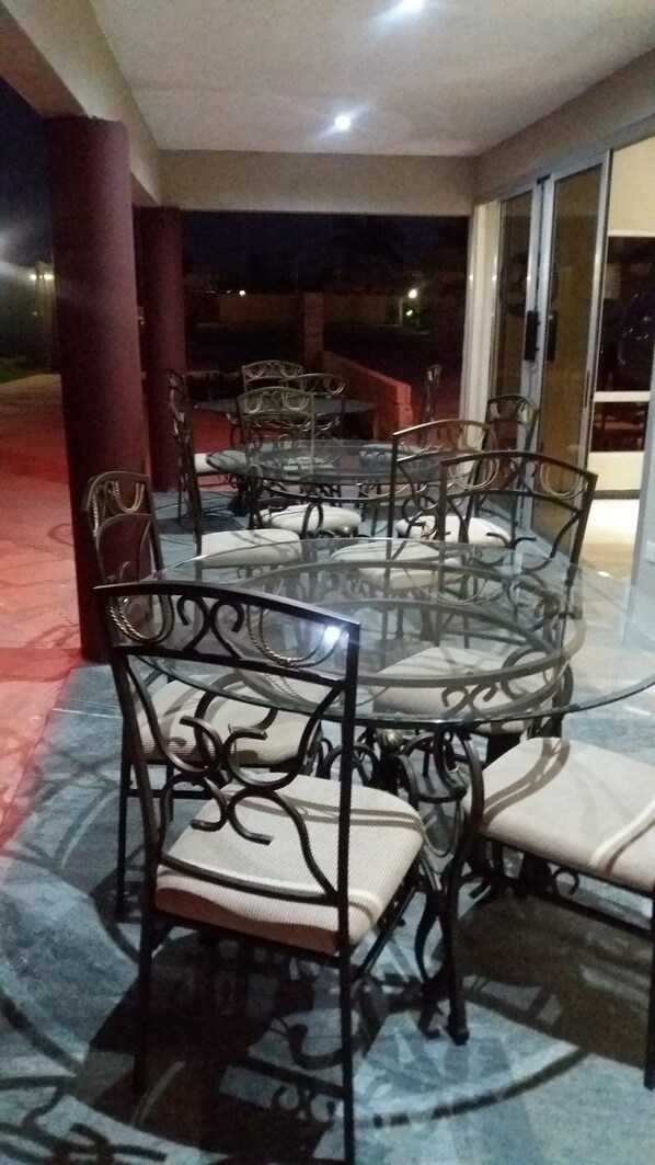 A round glass table with metal chairs and white cushions, set on a tiled floor with a red border. -  Purple Rose Boutique Hotel (Lusaka)