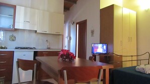 Une cuisine compacte avec un coin repas, une petite télévision et un lit recouvert d’une housse verte.
