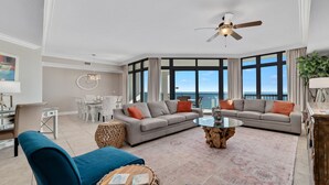 A spacious living room with a large window, a ceiling fan, and a dining area with a white table and chairs. - 5th Floor!!  Oasis, Formerly West II, New Owner, New to the Rental Market! (Orange Beach)
