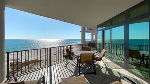 A balcony with a table and chairs, overlooking a beach and the ocean.