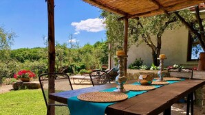 Une terrasse extérieure avec une table en bois dressée pour le repas, entourée de chaises et d’une pergola.