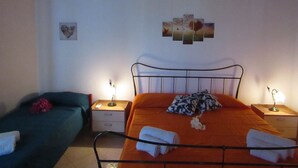 Un dormitorio con estructura de cama de metal, dos mesitas de noche con lámparas, un sofá verde, y una pared decorada con un adorno en forma de corazón y una pintura de paisaje.