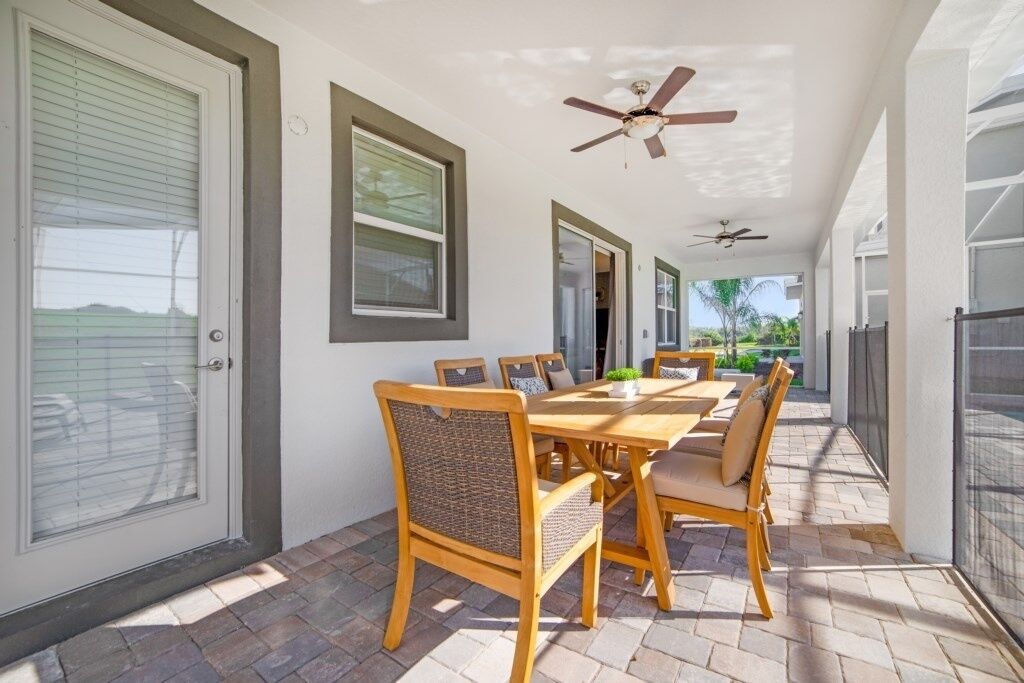 A covered patio with a dining table and chairs, ceiling fans, and a view of the outdoors.