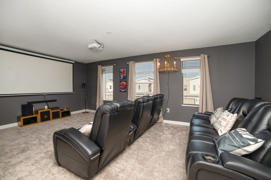 A home theater room with a large screen, reclining chairs, and a carpeted floor.