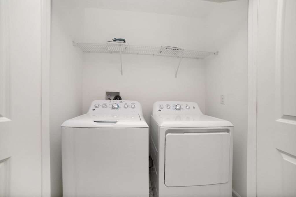 A laundry room with two front-loading washing machines and a metal shelf above them.