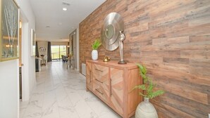 Un pasillo con pared de madera, suelo de mármol, un mueble de madera con cajones, un espejo redondo y una planta en maceta.