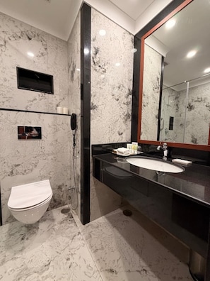 Een badkamer met een marmeren vloer, toilet, een zwart aanrecht met een wastafel, een spiegel en een douchehoek.