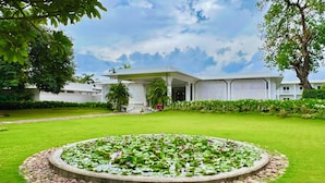Un edificio moderno con un estanque circular en primer plano, rodeado de un césped cuidado y una variedad de plantas.
