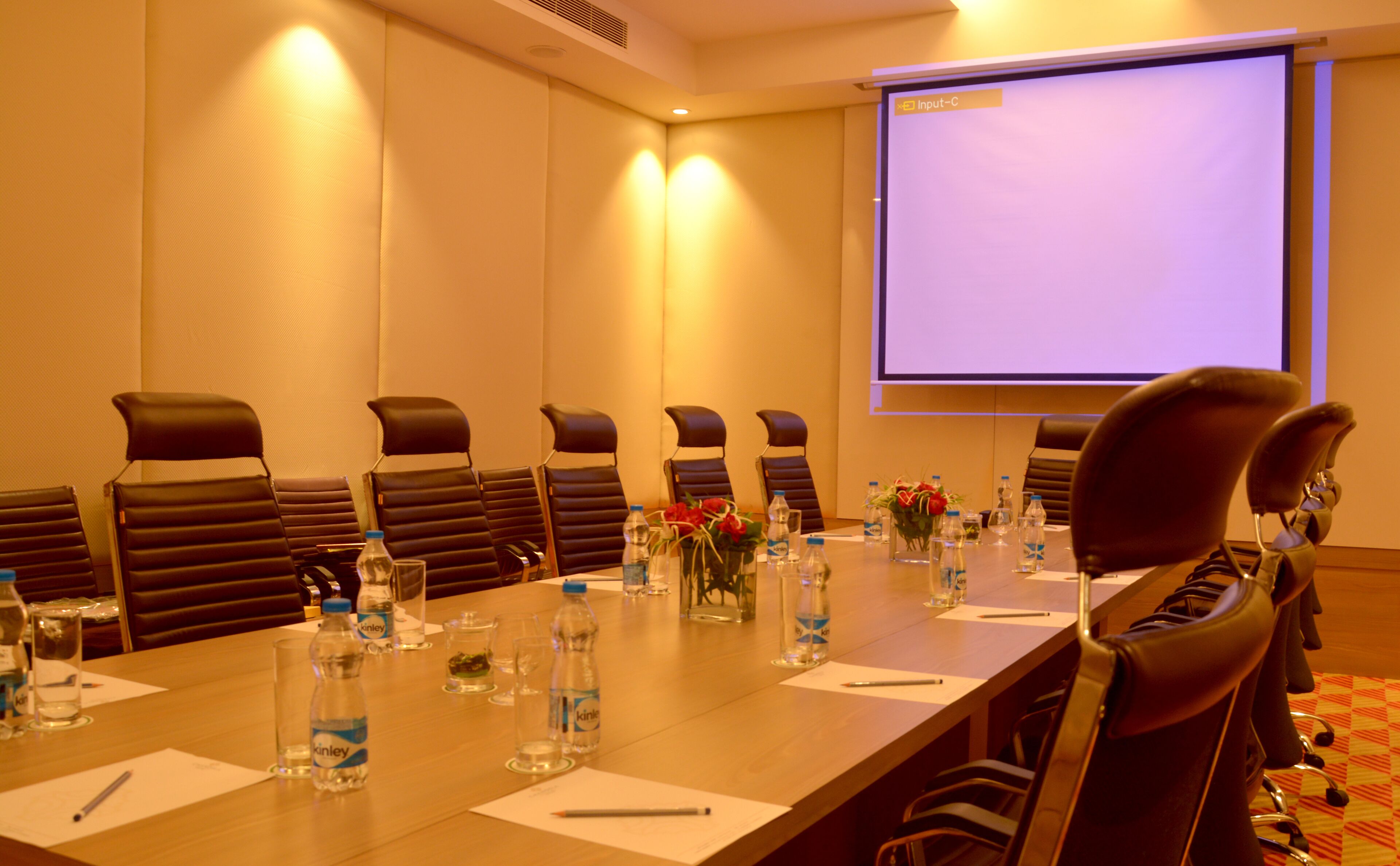 A conference room with a long table, chairs, water bottles, and a projector screen.