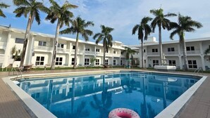 Una piscina con un flotador de dona rosa, rodeada de palmeras y un edificio blanco con balcones.