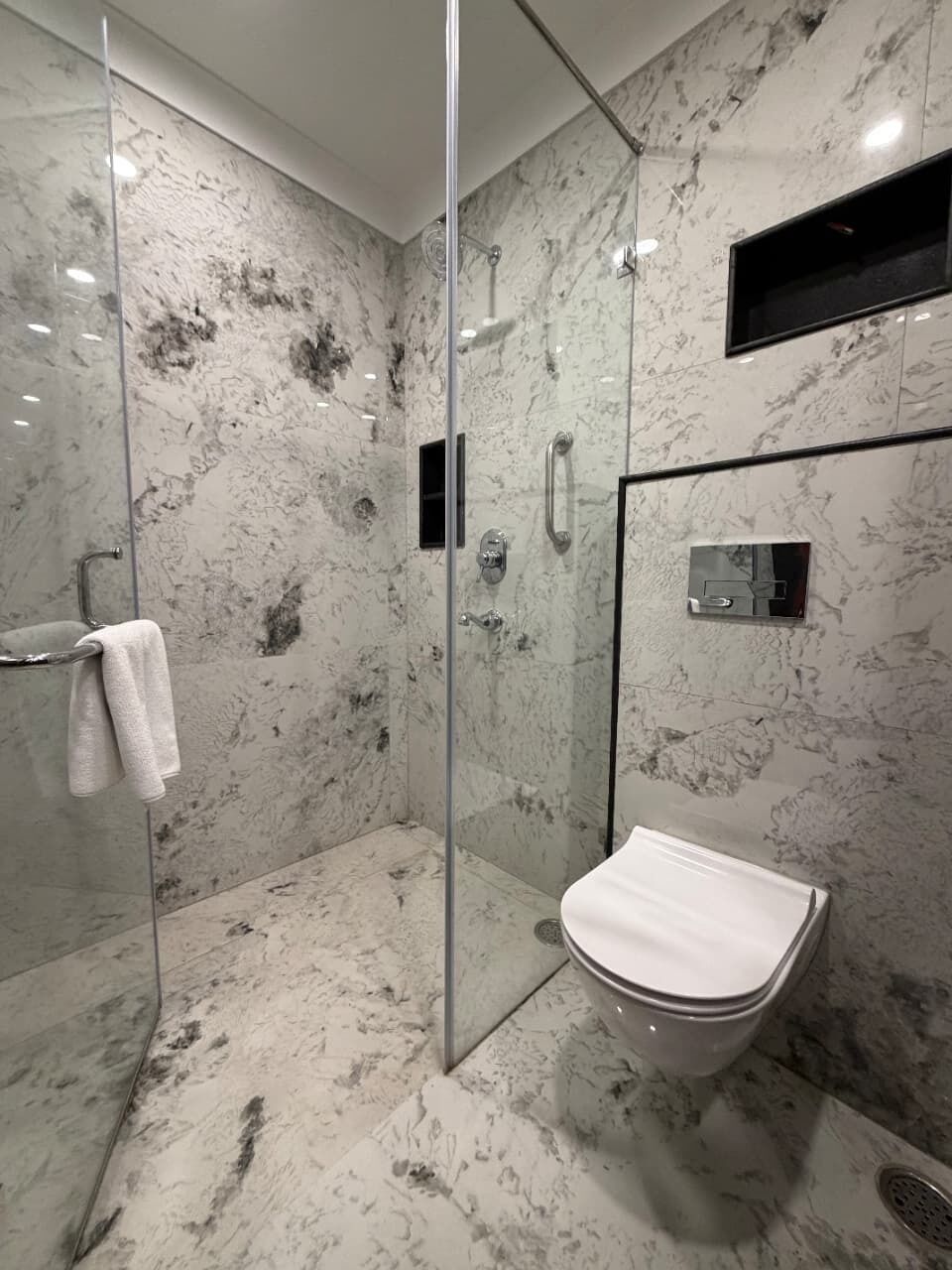 Un baño moderno con ducha de cristal, inodoro blanco y pared de mármol.