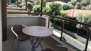Varanda com móveis de vime, uma mesa redonda e vista para uma paisagem montanhosa com árvores e edifícios.