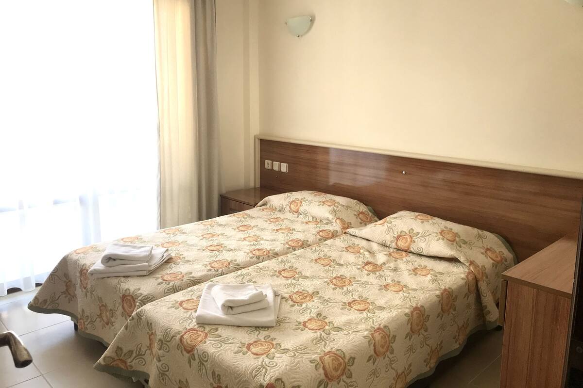 A hotel room with two beds, each with floral-patterned bedding and folded towels.