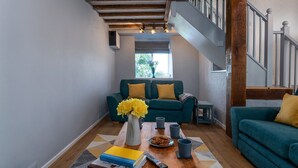 A living room with a sofa, a coffee table with books, a vase with flowers, and a staircase. - Converted Barn. Dogs welcome. Dog play field. Walk to local pub. (Tywyn)
