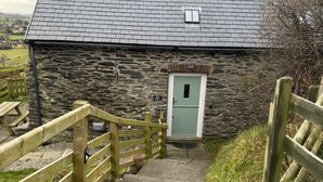 A stone building with a slate roof, a wooden staircase leading to a door, and a sign reading "The Inn". - Converted Barn. Dogs welcome. Dog play field. Walk to local pub. (Tywyn)