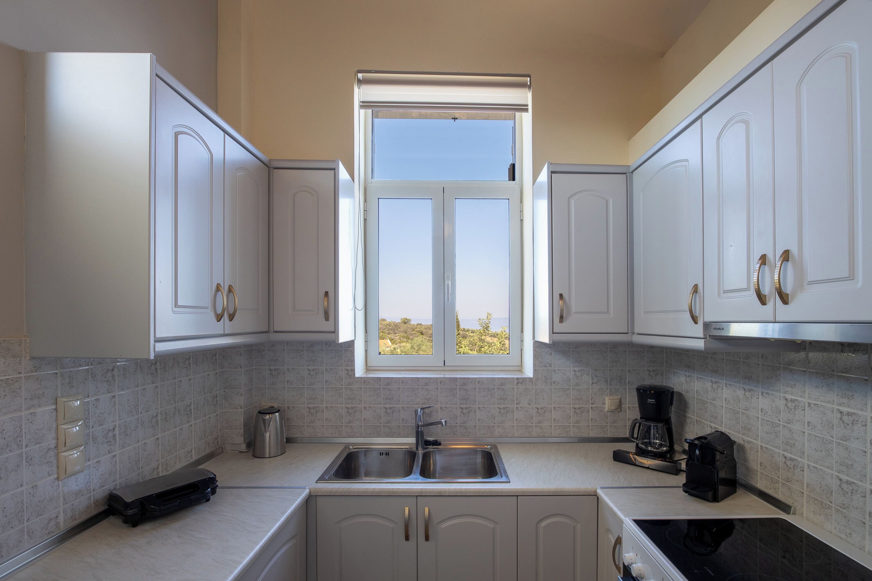 A modern kitchen with white cabinets, a double sink, and a window with a view.