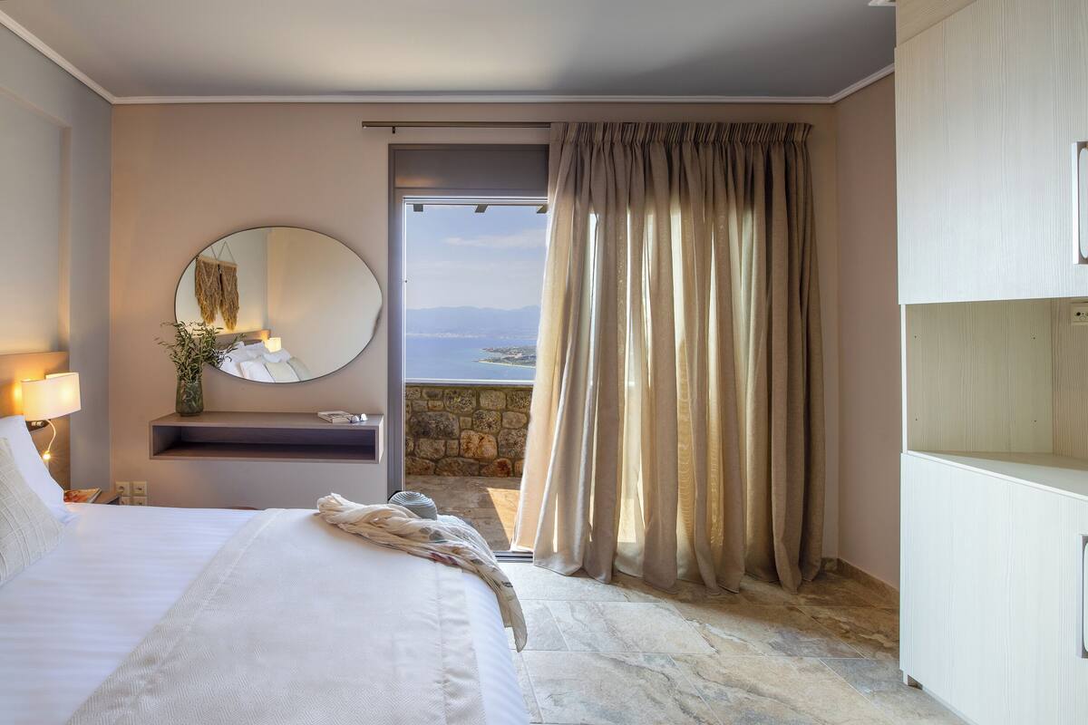 A hotel room with a bed, a round mirror, a small sink, and a view of the sea.
