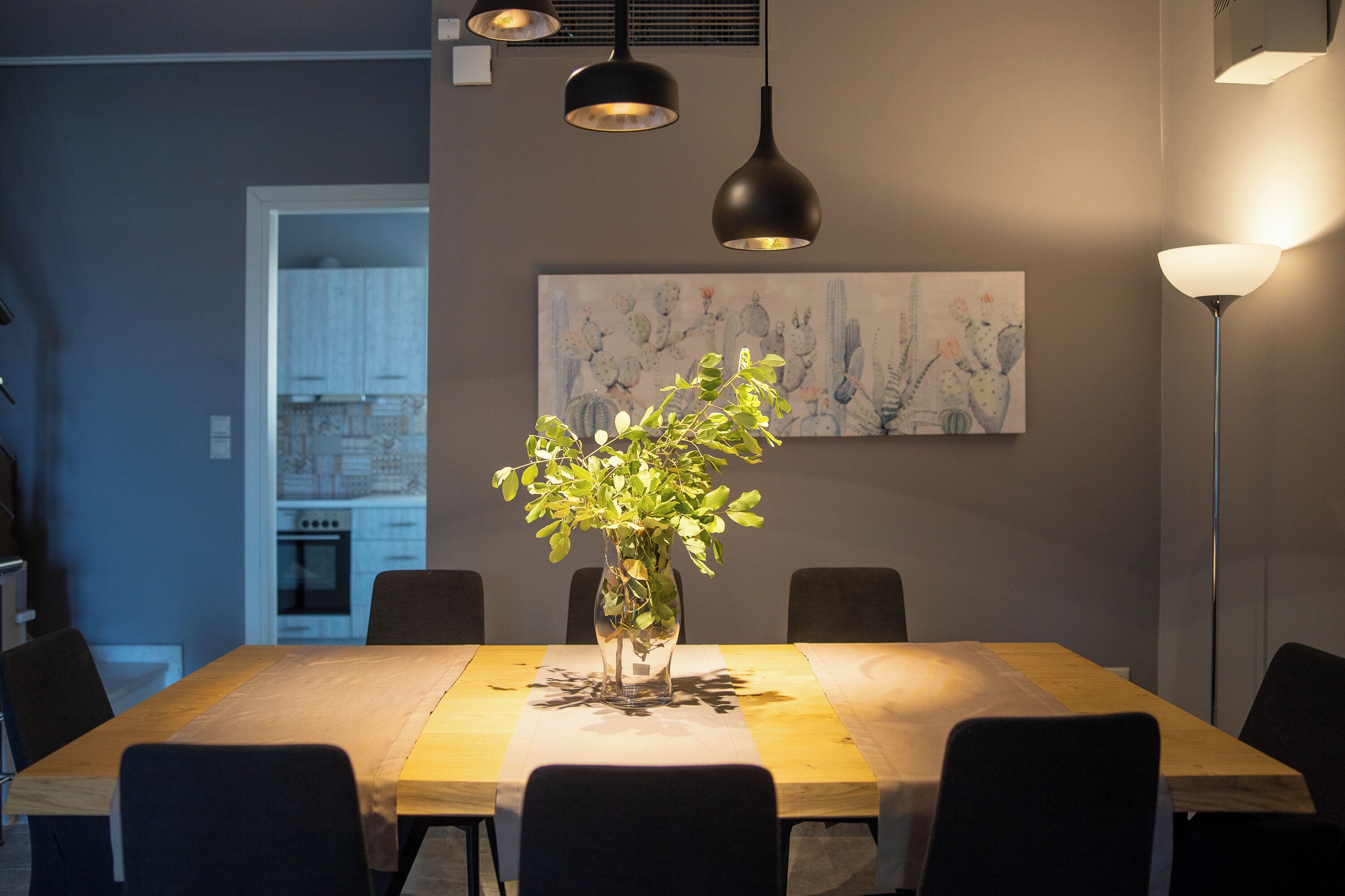Un coin repas avec une table en bois, des chaises noires, un vase contenant des plantes vertes et un tableau accroché au mur.
