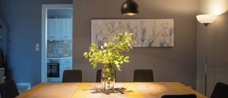 Un coin repas avec une table en bois, des chaises noires, un vase contenant des plantes vertes et un tableau accroché au mur.