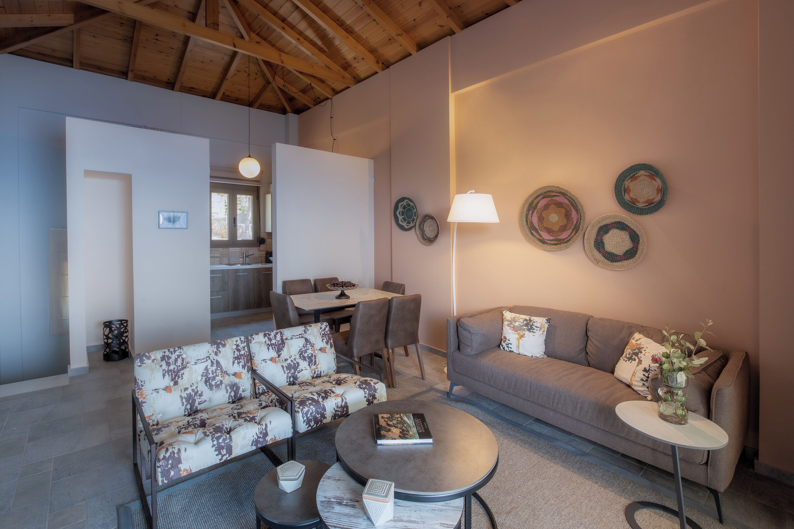 A modern living room with a sofa, armchair, coffee table, and a dining area with chairs and a table.