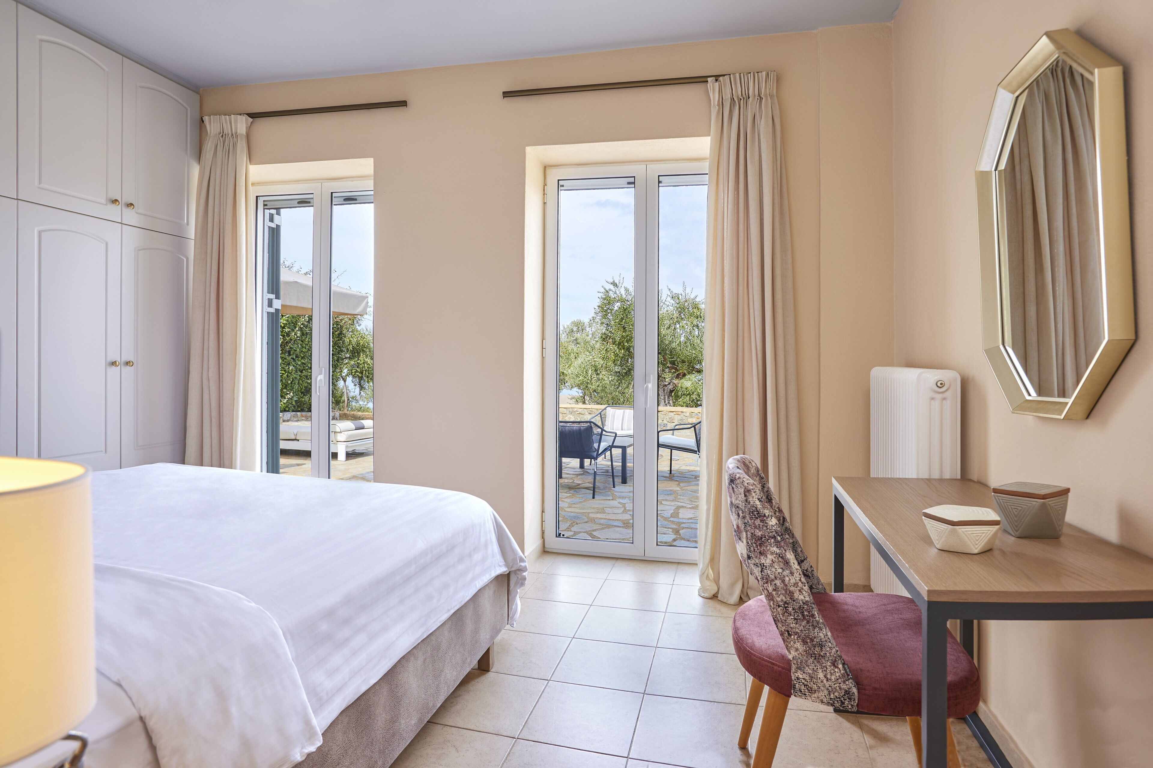 A hotel room with a bed, a desk, a chair, a mirror, and a view of the outdoors.