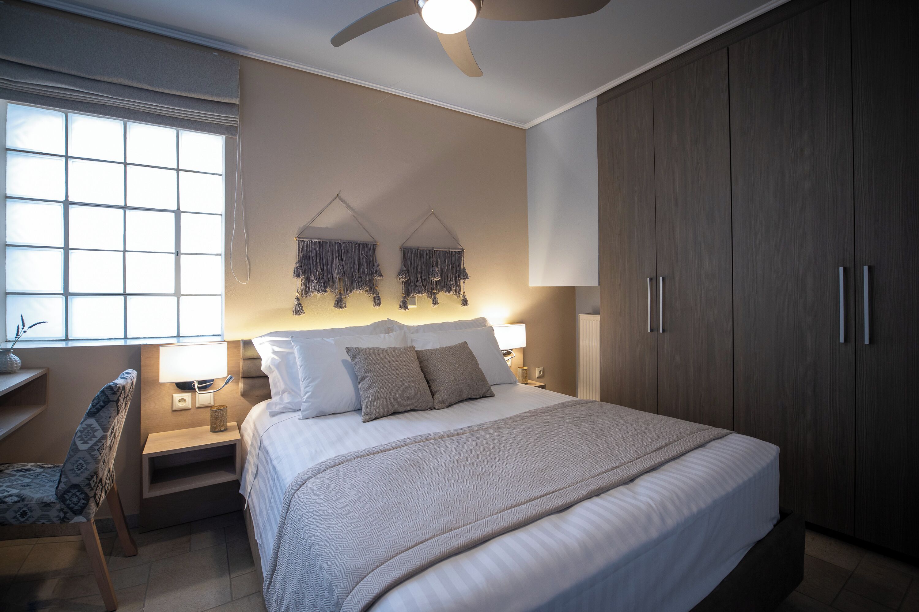 Une chambre avec un grand lit, des lampes de chevet, un ventilateur de plafond et une fenêtre avec des stores.