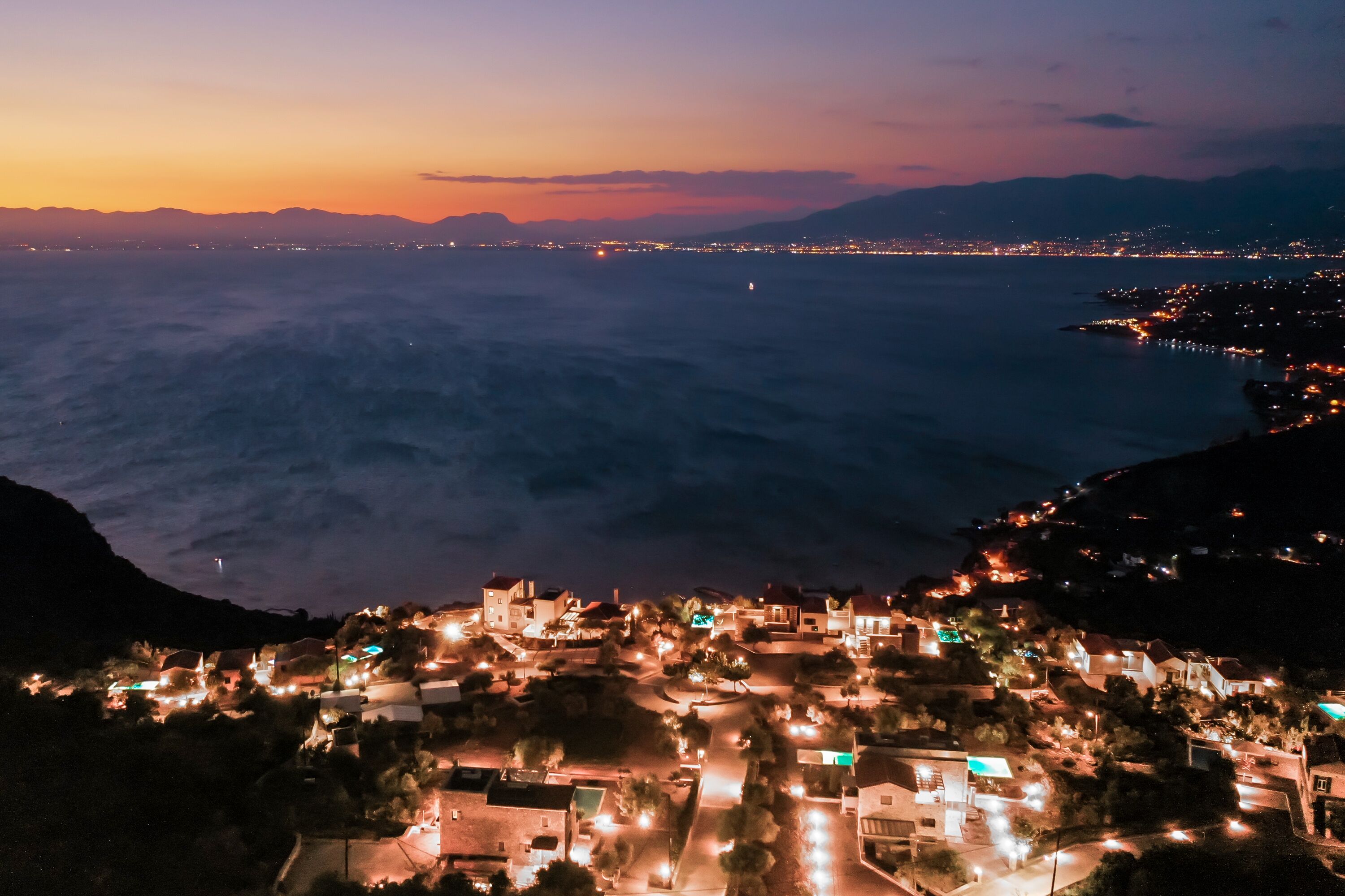 A coastal town at dusk with illuminated buildings and a view of the sea.