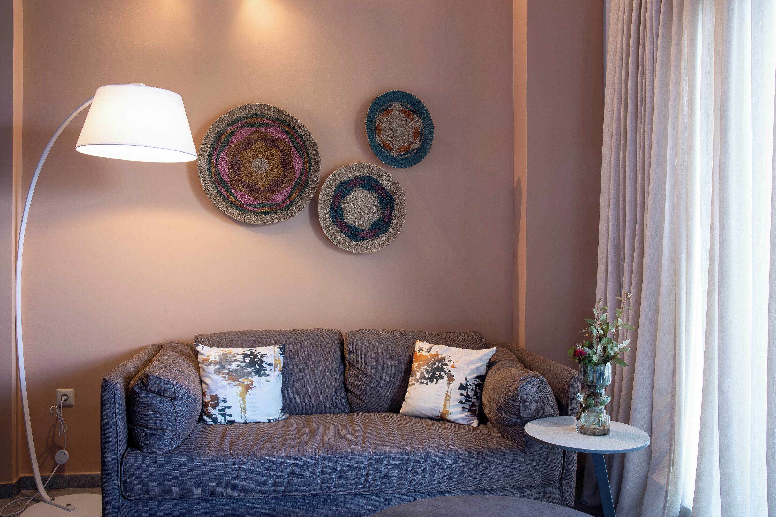 A grey sofa with two decorative pillows, a floor lamp, and three wall art pieces.