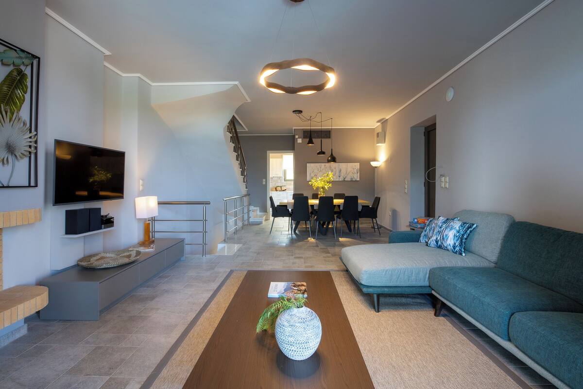 A modern living room with a sofa, a coffee table, and a TV. There is a staircase leading to an upper level.