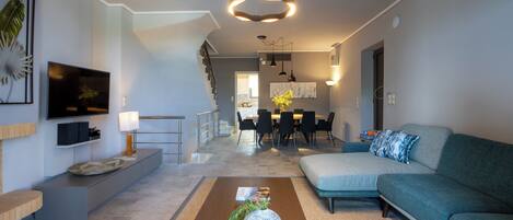 A modern living room with a sofa, a coffee table, and a TV. There is a staircase leading to an upper level.