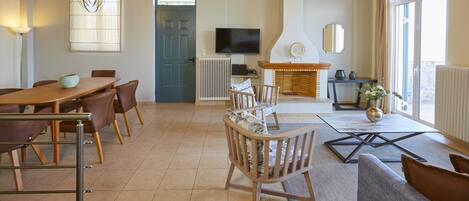 A spacious room with a wooden dining table, chairs, a sofa, and a television.