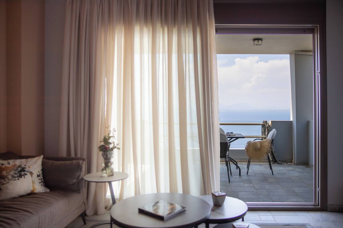 A room with a sofa, a small table, and a view of the sea through a balcony door.
