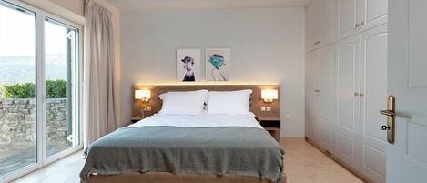 Un dormitorio con cama, ventilador de techo, mesita de noche, lámparas de pared y puerta corrediza que da a un balcón.