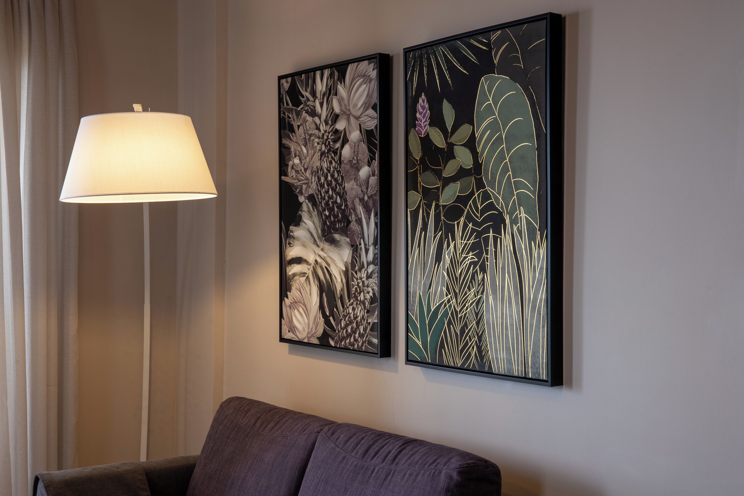 A room with a modern lamp, a sofa, and two framed botanical prints on the wall.