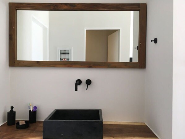 Un baño con un espejo grande, grifo negro y lavamanos negro.
