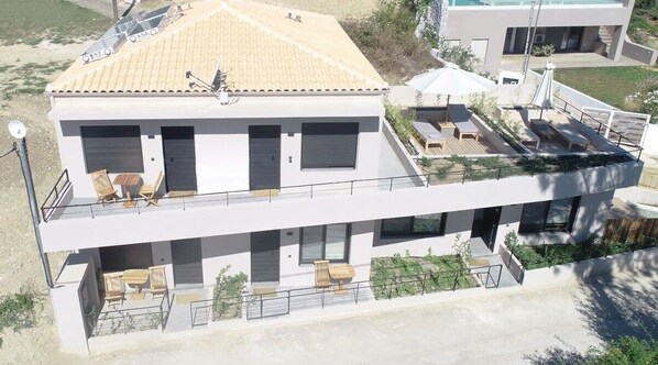 A modern two-story building with a flat roof, large windows, and a balcony with outdoor seating. - Elsa Modern Apartment One bed with private outdoor seating. Ground level Apt1 (Pogonia)