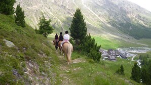 A group of people riding horses on a mountain trail with a view of a valley and a building complex in the background. - Wonderful apartment inside the top residence kurz (Maso Corto)