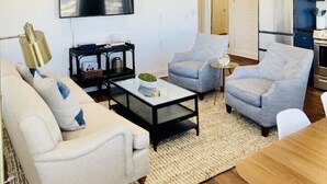 Una sala de estar moderna con un sofá, dos sillones, una mesa de centro y un televisor de pantalla plana montado en la pared.