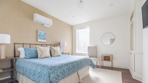 Un dormitorio con cama, mesitas de noche, lámpara, espejo, ventana con persianas y equipo de aire acondicionado.