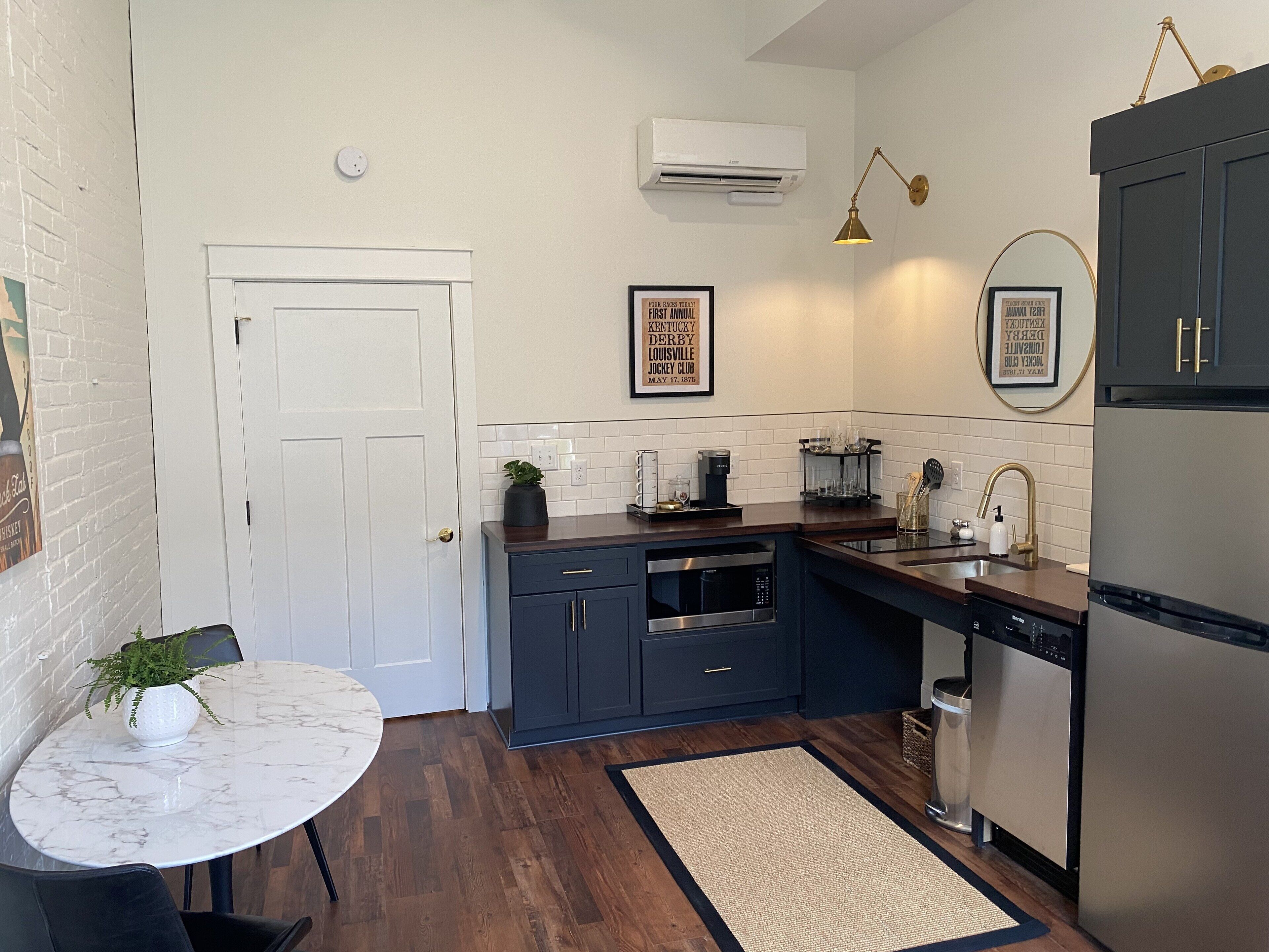 Une cuisine moderne avec des meubles de couleur sombre, un crédence en carreaux blancs, un four encastré et un réfrigérateur en acier inoxydable.