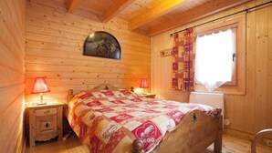 A wooden cabin bedroom with a bed, two bedside lamps, a clock, and a window with curtains. - Chalet Anais, traditional Alpine feel (Montgenevre)