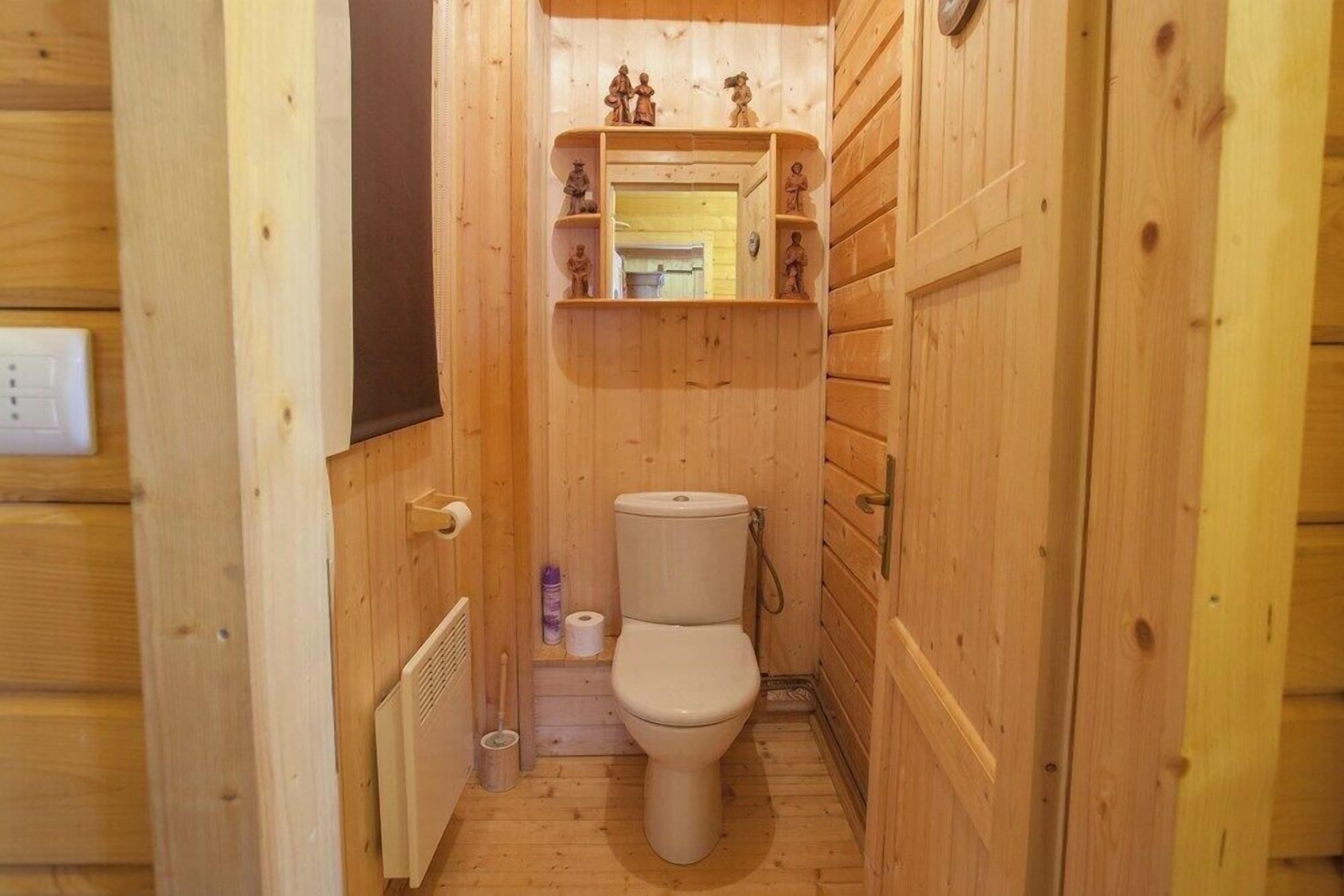 A wooden bathroom with a toilet, a shelf with figurines, and a mirror.