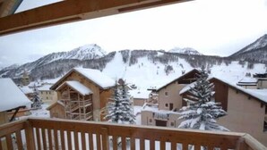 A wooden balcony with a view of snow-covered buildings and mountains. - Chalet Anais, traditional Alpine feel (Montgenevre)