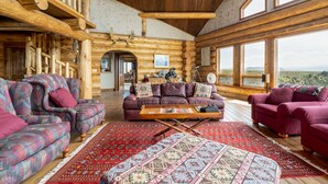 A log cabin interior with a large window, a sofa, a coffee table, and a patterned rug. - Arrowhead Lodge -Secluded home with incredible views and now Air Conditioning (Livingston)