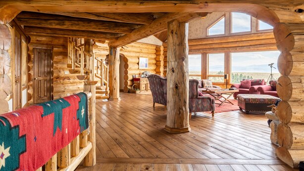 A log cabin interior with a wooden staircase, a large window offering a view, and a cozy seating area with a red blanket. - Arrowhead Lodge -Secluded home with incredible views and now Air Conditioning (Livingston)