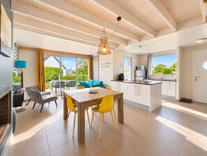 A modern kitchen with a dining area, large windows, and a view of greenery.