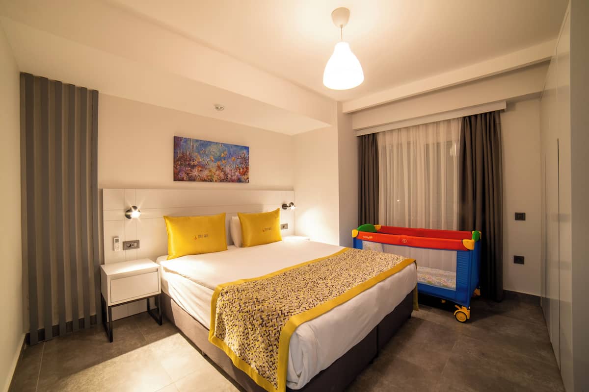 A hotel room with a bed, bedside tables, a wall-mounted painting, curtains, and a crib.