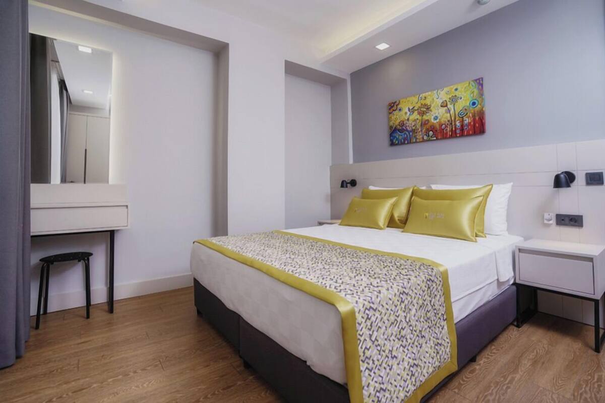 A modern hotel room with a bed, bedside tables, a desk, and a mirror.