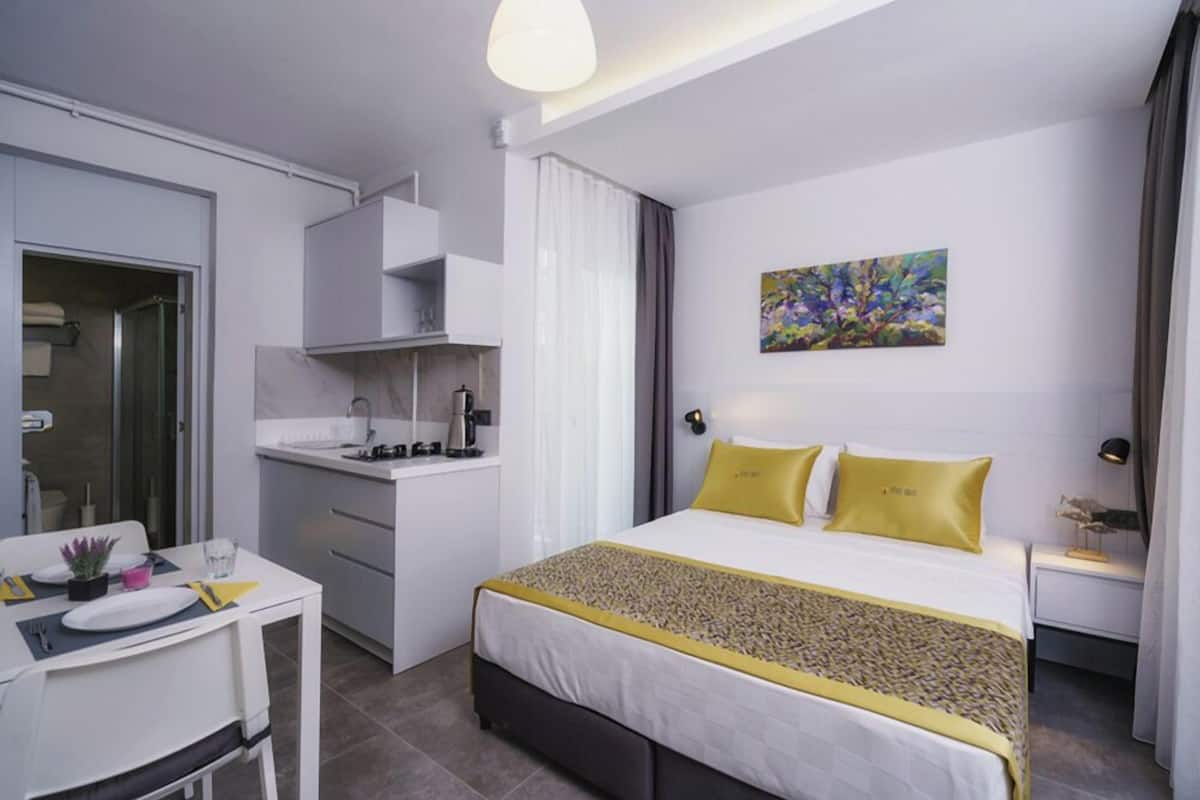 A modern hotel room with a bed, bedside table, and a small kitchenette.